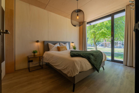 Moderne slaapkamer in Forest Villa bij Holiday Park BreeBronne, Nederland, met groot raam naar de natuur.