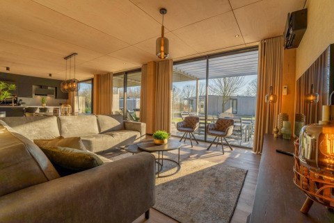 Moderne woonkamer in Forest Villa op Holiday Park BreeBronne, Nederland, met grote ramen en sfeervolle inrichting.