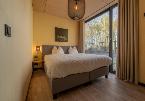 Knusse slaapkamer in Forest Villa bij Holiday Park BreeBronne, Nederland, met groot bed en bosuitzicht.