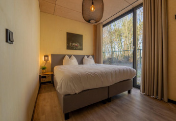 Cozy bedroom in the Forest Villa at Holiday Park BreeBronne, Netherlands, with large bed and forest view.