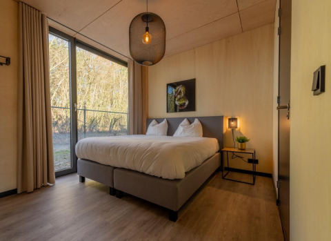Slaapkamer in een Forest Villa-lodge bij BreeBronne met tweepersoonsbed, groot raam en sfeervol interieur.