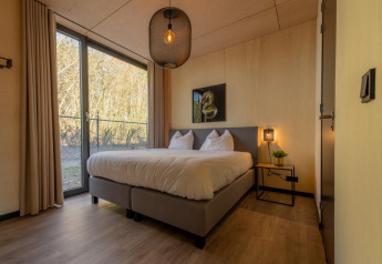 Slaapkamer in een Forest Villa in vakantiepark BreeBronne met groot raam, tweepersoonsbed en modern interieur.