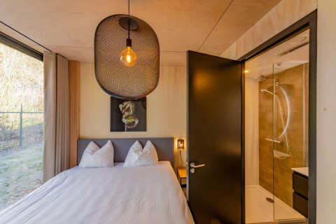 Slaapkamer met tweepersoonsbed, groot raam en badkamer in Forest Villa, Holiday Park BreeBronne, Nederland.