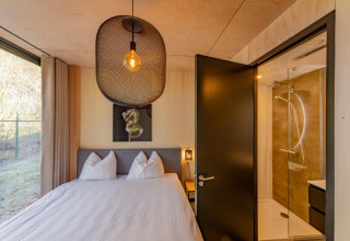 Slaapkamer met tweepersoonsbed, groot raam en badkamer in Forest Villa, Holiday Park BreeBronne, Nederland.