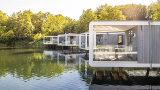 Moderni lodge Water Cube su palafitte sopra un lago tranquillo, circondati da alberi e acqua riflettente.