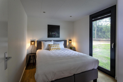 Moderne slaapkamer in de Water Cube-lodge van Holiday Park BreeBronne, Nederland, met tweepersoonsbed en tuinzicht.