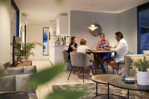 Gezin dineert samen aan tafel in een moderne lodge bij Water Cube, Holiday Park BreeBronne, Nederland.