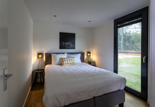 Moderne slaapkamer in de Water Cube-lodge bij Holiday Park BreeBronne, met groot bed en tuinzicht.