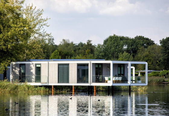 Moderne Water Cube lodge op een rustig meer, omgeven door groen, weerkaatst in het water.