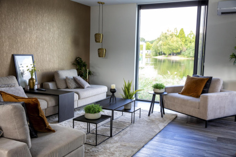 Moderne woonkamer in de Water Cube-lodge met groot raam, uitzicht op meer en stijlvol interieur in BreeBronne.