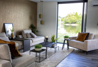 Moderne woonkamer in de Water Cube-lodge met groot raam, uitzicht op meer en stijlvol interieur in BreeBronne.