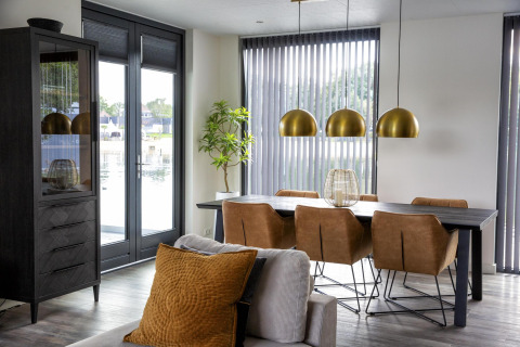 Moderne eethoek in Water Cube-lodge, BreeBronne, Nederland met bruine stoelen, zwarte tafel en grote ramen.