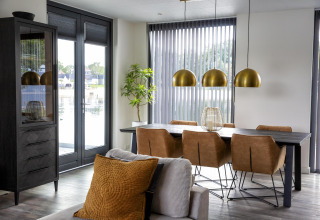 Moderne eethoek in Water Cube-lodge, BreeBronne, Nederland met bruine stoelen, zwarte tafel en grote ramen.