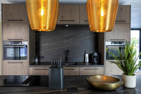 Moderne keuken in de Water Cube-lodge, BreeBronne, Nederland, met hout, zwart blad en gouden hanglampen.