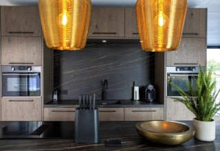 Moderne keuken in de Water Cube-lodge, BreeBronne, Nederland, met hout, zwart blad en gouden hanglampen.