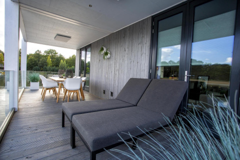 Moderne terras met ligstoelen en eettafel bij Water Cube lodge in Holiday Park BreeBronne, Nederland.