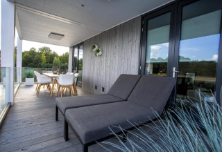 Moderne terras met ligstoelen en eettafel bij Water Cube lodge in Holiday Park BreeBronne, Nederland.
