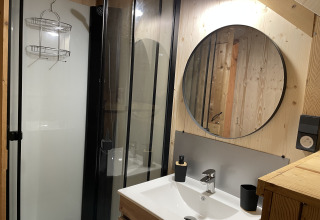 Salle de bain moderne avec miroir rond et douche à la Safari Lodge « All Season » au Chianti Glamping Resort, Italie.