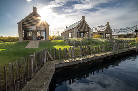 Foto di moderni lodge in legno a Villa Oesterdam, affacciati sull'acqua con prato verde e sole.