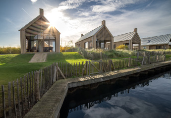 Foto moderner Holzhütten bei Villa Oesterdam am Wasser, umgeben von Natur und Sonnenlicht.
