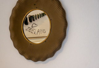 Runder Spiegel mit goldenem Rahmen, reflektiert Flaschenkunst und das Wort 'ZEELAND' in Villa Oesterdam.
