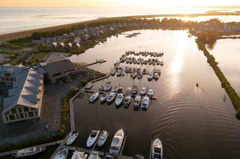 Luftaufnahme von Villa Oesterdam Glamping mit Yachthafen, Booten, Häusern und See im Sonnenuntergang.