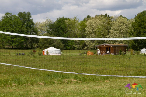 Vista su una rete da pallavolo, una yurta e una casetta di legno a Domaine EcÔtelia in Nouvelle-Aquitaine, Francia.