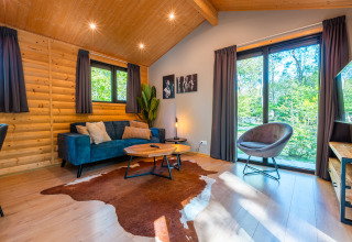 Sala de estar en la cabaña Velthorst del parque vacacional De Wiltzangh, Países Bajos, con grandes ventanales.