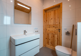 Moderne badkamer in lodge 'Velthorst' op vakantiepark De Wiltzangh, Nederland, met houten deur en witte tegels.