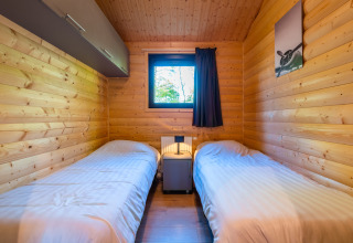 Gemütliches Schlafzimmer mit zwei Einzelbetten, Holzverkleidung und Fenster in der Velthorst-Lodge, De Wiltzangh.