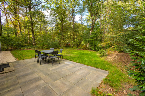 Paved patio with outdoor dining set at Velthorst lodge in De Wiltzangh holiday park, Netherlands, forest backdrop.