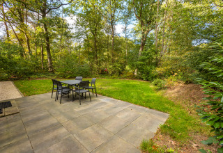 Patio lastricato con set da pranzo esterno al lodge Velthorst nel parco De Wiltzangh, Paesi Bassi, vista bosco.