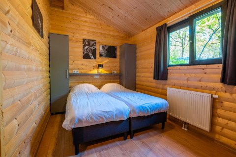Knusse houten slaapkamer met twee eenpersoonsbedden, kasten en raam in Velthorst-lodge, De Wiltzangh.