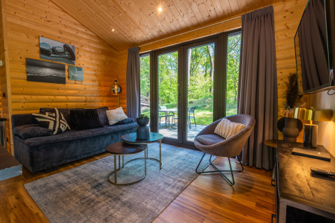 Salón en la Wellness Lodge «Wood XL» en Holiday park De Wiltzangh, con sofá moderno y ventanales al jardín.