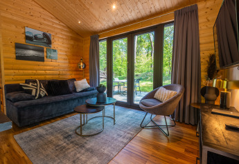 Living room of Wellness Lodge «Wood XL» at Holiday park De Wiltzangh, featuring cozy sofa and garden view.