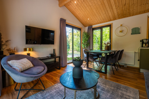 Moderne leefruimte met eetplaats in Wellness Lodge ‘Wood XL’ met zicht op natuur in De Wiltzangh, Nederland.