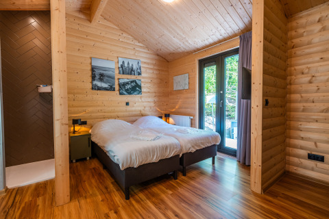 Dormitorio en Wellness Lodge «Wood XL» con paredes de madera, dos camas y acceso a terraza en Holiday park De Wiltzangh.