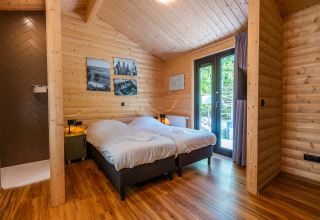 Dormitorio en Wellness Lodge «Wood XL» con paredes de madera, dos camas y acceso a terraza en Holiday park De Wiltzangh.