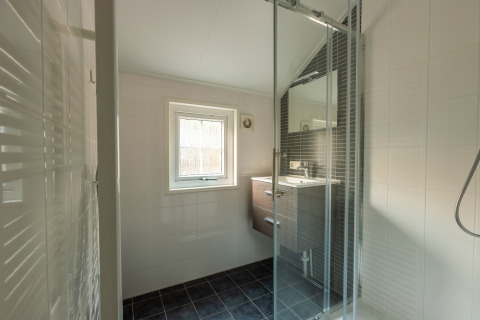 Bagno moderno con doccia in vetro, piastrelle scure e finestra nella tiny house Heidelodge a De Wiltzangh.