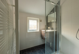 Modernes Bad im Heidelodge Tiny House mit Glasdusche, dunklen Bodenfliesen und Fenster in De Wiltzangh.