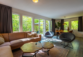 Salón en chalet finlandés del parque De Wiltzangh en Países Bajos, con sofá, sillones y mesa de comedor.