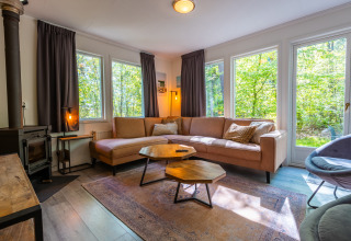 Woonkamer van een Fins Chalet op De Wiltzangh, Nederland, met hoekbank, grote ramen en boszicht.