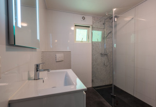 Salle de bain moderne avec douche, lavabo, miroir et fenêtre au Finnish Chalet, De Wiltzangh, Pays-Bas.