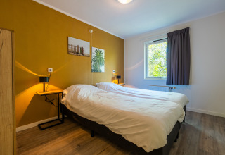 Soveværelse i en finsk chalet på ferieparken De Wiltzangh i Holland med dobbeltseng og gul væg.