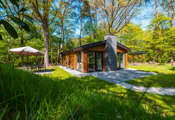 Moderne Hackfort-lodge in het bos, met grote ramen, terras en zithoek met parasol buiten.