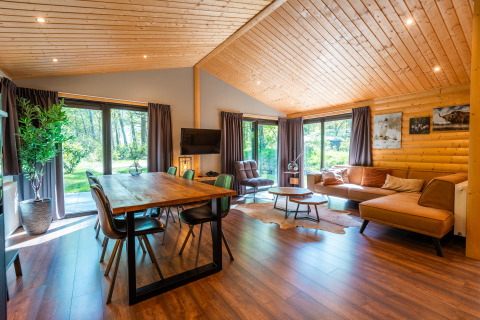 Interno luminoso e moderno di un lodge con pareti in legno, zona pranzo, divano e grandi finestre a De Wiltzangh.