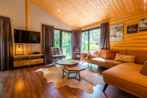 Gezellige houten woonkamer in lodge ‘Hackfort’ bij Holiday park De Wiltzangh in Nederland, met grote ramen.
