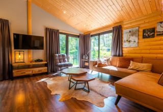 Cozy wooden lodge living room at Hackfort in Holiday park De Wiltzangh, Netherlands, with large windows.