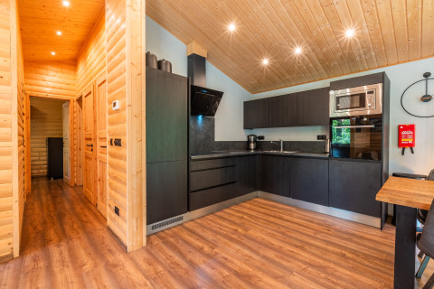 Cucina moderna in lodge con mobili neri a L, pareti in legno, pavimento in legno e illuminazione.
