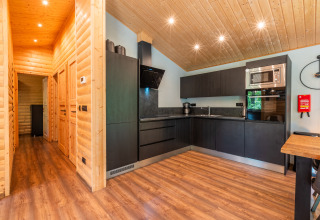 Moderne lodgekeuken met L-vorm, zwarte kasten, houten muren en vloer, en plafondverlichting.